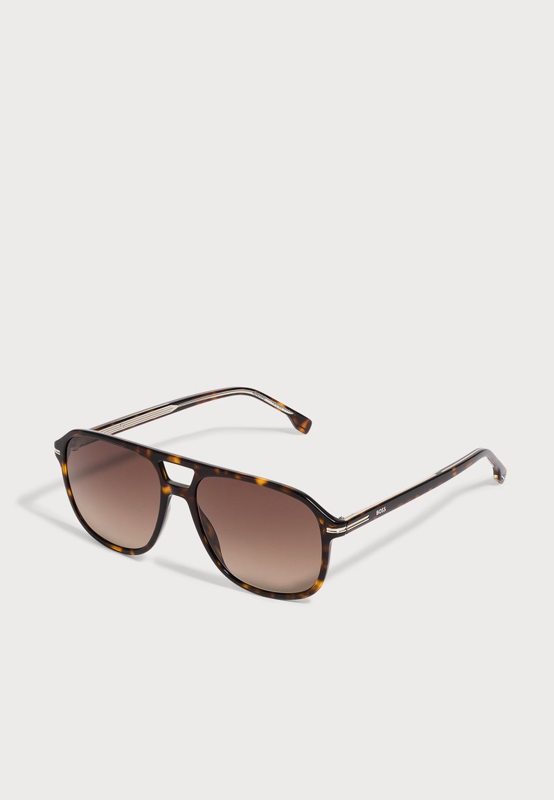 Lunettes de soleil aviateur en écaille avec verres dégradés marron et branches fines, présentées sur une surface blanche.