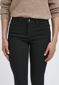 Juodi siauri džinsai, pagaminti iš lygaus tekstūros džinsinio audinio. Savybės: penki kišenės, priekinis mygtukas ir prigludęs dizainas.