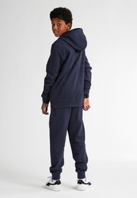 Sudadera azul marino y pantalones de chándal a juego, hechos de tela suave. Presenta una capucha, puños acanalados y dobladillo elástico. Acentuado con zapatillas blancas.