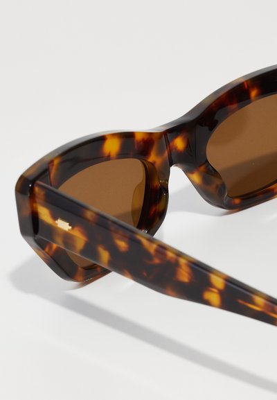 Tortoiseshell sunglasses with brown tinted lenses. Chunky plastic frame features a geometric design and smooth finish, enhancing durability.