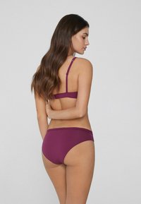 Fialkové bikiny s tenkými ramínky a bezešvým designem, které zdůrazňují hladkou texturu a klasický, minimalistický střih.