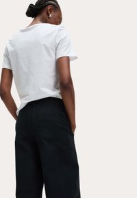 Witte t-shirt met korte mouwen gecombineerd met zwarte hoge taillebroek met achterzakken en een rechte pasvorm. Eenvoudige achtergrond.