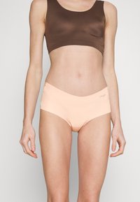 Light peach seamless underwear with an elastic waistband, featuring a smooth texture and minimalistic design, accompanied by a brown crop top.