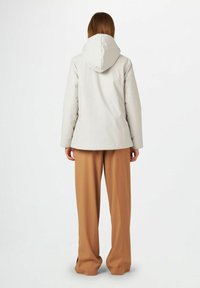 Veste à capuche beige clair avec une texture lisse et une coupe décontractée, associée à un pantalon marron ample. Design minimaliste, sans éléments métalliques visibles.