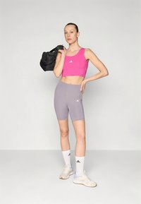 Sportska odjeća koja uključuje ružičasti kratki top i sive biciklističke kratke hlače, oba s Adidas logotipom. Stilizirano s bijelim čarapama i bež tenisicama.