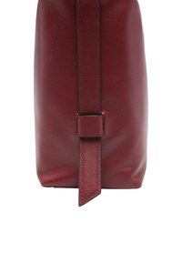 Borsa in pelle rossa scura vista laterale con una cinghia verticale cucita infilata in un supporto in pelle abbinato.