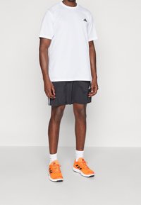 Camiseta atlética blanca de manga corta, pantalones cortos negros y zapatillas de correr naranja brillante con detalles en negro, acompañadas de calcetas atléticas blancas.