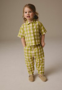 Chemise à manches courtes à carreaux verts et beiges avec un pantalon assorti, fabriquée en tissu léger, associée à des chaussures beiges.