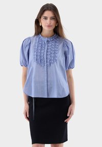 Blau-weiß gestreifte Bluse mit Puffärmeln, mit einem gerafften Frontdesign und einem Rundhalsausschnitt, kombiniert mit einem schwarzen Bleistiftrock.