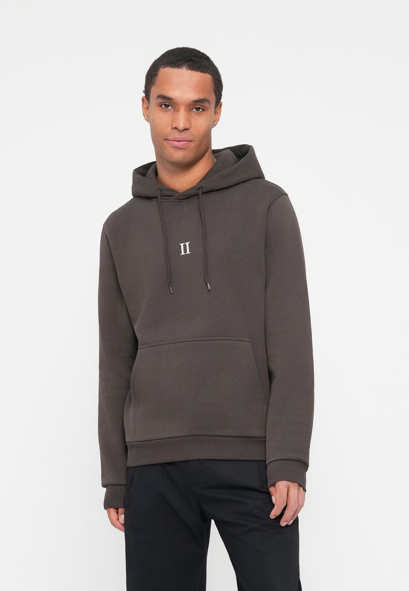 Sweat à capuche marron en tissu mélangé coton, avec une poche frontale, des cordons de serrage et un petit logo blanc sur la poitrine. Design simple et décontracté.