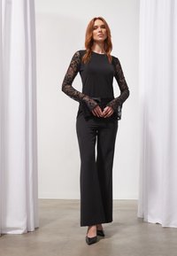 Haut noir à manches longues avec des accents en dentelle, associé à un pantalon large. Tissu lisse avec des détails en dentelle visibles sur les manches, complété par des talons noirs.