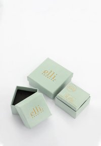 Trois boîtes à bijoux vert clair avec le logo doré "elli premium", dont une ouverte dévoilant un intérieur noir, posées sur une surface blanche.