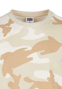 Beige camouflage t-shirt med abstrakte former i nuancer af tan og creme. Fremstillet i bomuld med rund hals og synlig mærkevarelabel.