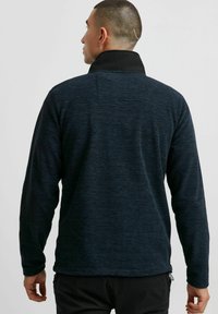 Fleece-Pullover in dunklem Farbton mit strukturiertem Stoff, einem schwarzen Kragen und verstellbarem Saum. Verfügt über einen geraden Schnitt mit langen Ärmeln.