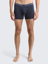 Männliches Model trägt navyblaue Tom Tailor Boxershorts und steht barfuß vor einem schlichten hellgrauen Hintergrund.