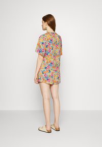 Macacão floral colorido com mangas curtas e um corte solto, feito de um tecido leve com padrões vibrantes em rosa, laranja e azul.