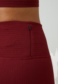 Burgunder ribbet stoff sportstopp med et elegant design, med en diskret glidelås på siden av den matchende høytlivs bunnen.