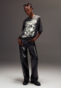 Crna grafička majica s dizajnom "Stranger Things", uparena s sjajnim crnim hlačama širokog kroja od umjetne kože i robustnim crnim čizmama.