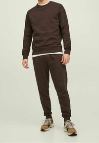 Mörkbrun bomullströja och matchande joggers, med rundad hals och ribbade ärmslut, tillsammans med flerfärgade träningssneakers.