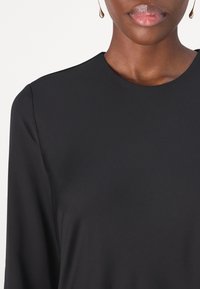 Crna, majica dugih rukava s okruglim izrezom. Glatka tkanina s elegantnim, minimalističkim dizajnom, koja prikazuje čistu siluetu bez ukrasa.