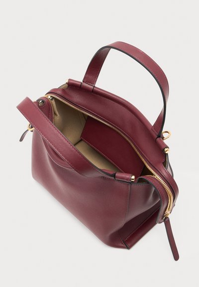 Sac à main en cuir bordeaux ouvert avec fermeture éclair dorée et doubles poignées, montrant un intérieur beige et une petite poche intérieure.
