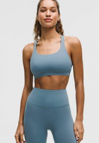 Brassière de sport bleu clair et leggings taille haute en tissu lisse et extensible. Dispose d'un col arrondi et de larges bretelles pour un bon maintien.