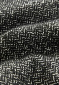 Struktuurne kangas, millel on herringbone-muster musta ja valge tooni, näidates pehmet, kudumist meenutavat välimust. Suumi vaade toob esile detailid.