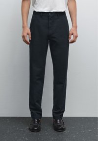 Pantaloni su misura blu scuro con vita piatta e passanti per cintura. Realizzati in un tessuto liscio, presentano tasche laterali e una tasca posteriore singola.