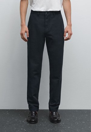 Pantalons ajustés bleu foncé avec une taille plate et des passants de ceinture. Fabriqués dans un tissu lisse, comportant des poches latérales et une seule poche arrière.
