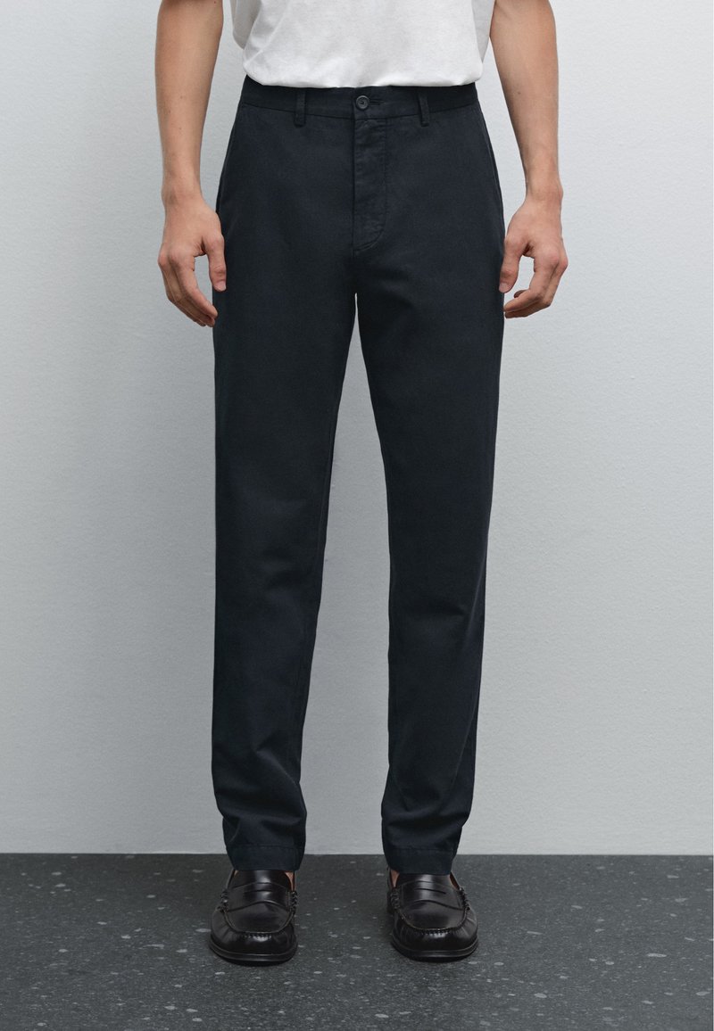 Pantaloni su misura blu scuro con vita piatta e passanti per cintura. Realizzati in un tessuto liscio, presentano tasche laterali e una tasca posteriore singola.