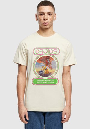 Jonge man met sproeten die een beige T-shirt draagt met retro Star Wars-droids R2-D2 en C-3PO met neon tekst en afbeelding.