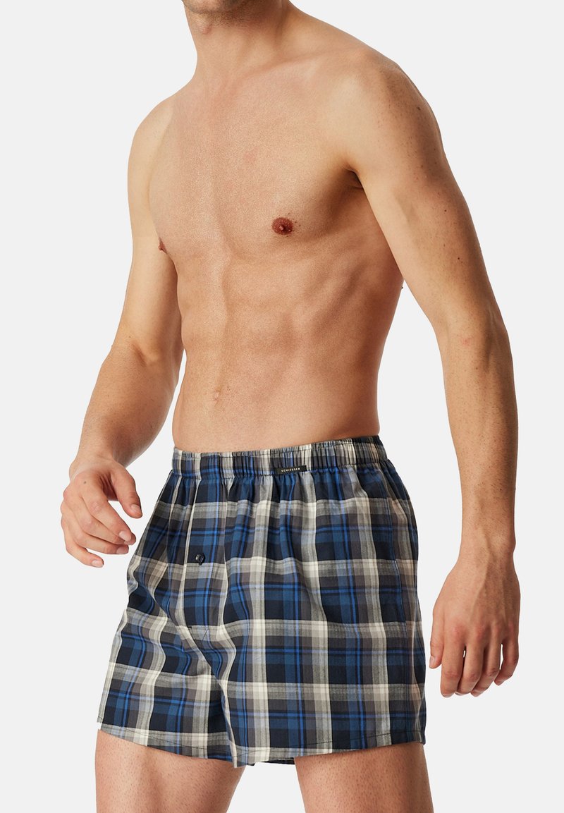 Boxer a scacchi caratterizzati da un design a quadri blu, bianco e grigio. Vita elastica con dettaglio a bottone. Tessuto leggero e traspirante.