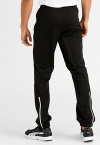 Svarta träningsbyxor med smal passform, elastisk midja och vita sidogylvar. Tillverkade av ett mjukt och lätt tyg med en mudd i nederkant.