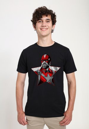 Sort t-shirt med et rød- og grågrafik af et skægget karakters hoved inden i en stjerneform, trykt på forsiden.