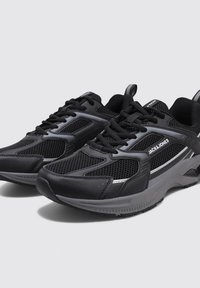 Baskets de sport noires avec des panneaux en maille, matériau synthétique texturé, fermeture à lacets, accents réfléchissants et semelle rembourrée.