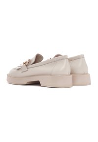 Mocassins en cuir beige avec une semelle à talon bas, dotés de quincaillerie décorative et de coutures. Texture lisse avec un design à bout rond.