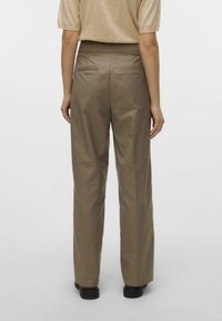 Pantaloni beige a gamba larga dal tessuto morbido, con vita alta e due tasche posteriori, abbinati a una blusa chiara e scarpe nere.