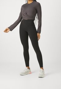 Black high-waisted leggings paired with a dark gray long-sleeve top featuring a twisted front design. Light gray sneakers with pink accents.
