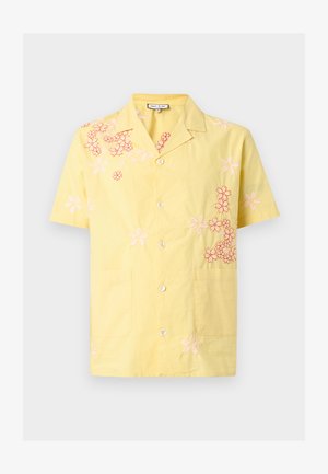Chemise jaune à manches courtes avec boutons, ornée de motifs floraux brodés rose et rouge, et deux poches à l'avant.