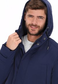 Chaqueta con capucha color azul marino, con cremallera frontal, puños elásticos, bolsillos laterales y textura suave. Cordón ajustable en la capucha.
