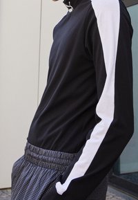 Czarna bawełniana bluzka z długim rękawem i białym paskiem na rękawie, w zestawie z kratkowymi spodniami z elastycznym pasem.