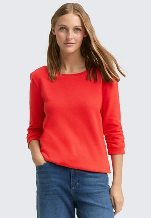Roter Pullover mit langen Ärmeln, rundem Ausschnitt und gerippten Bündchen, kombiniert mit blauen Jeans. Weicher Stoff, schlichtes Design und figurbetonte Passform.
