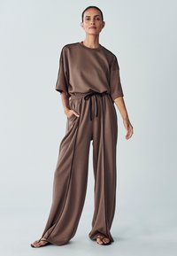 Brown lounge set featuring a loose-fit short-sleeve top with black trim, and wide-leg pants with an adjustable drawstring waist and pockets.