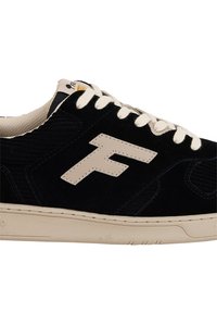 Sneaker nera in suede con lacci crema, caratterizzata da un grande logo beige sul lato, materiali testurizzati e una suola di gomma chiara.