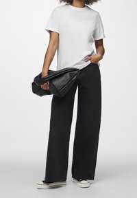 Vit bomull t-shirt, lös passform, tillsammans med svarta vida jeans. Modellen håller en stor svart strukturerad väska och bär svarta sneakers.