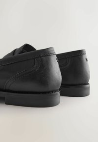 Pantofi negri din piele cu finisaj texturat, având un design neted și tălpi negre rezistente. Cusăturile detaliate de-a lungul marginilor sunt vizibile.