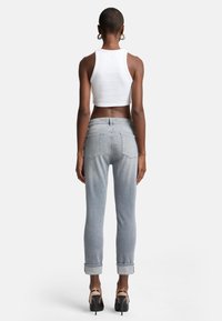 Lichtgrijze high-waisted jeans met opgerolde cuffs, achterzakken en een gladde afwerking. Gecombineerd met een witte cropped tanktop en zwarte hakken.
