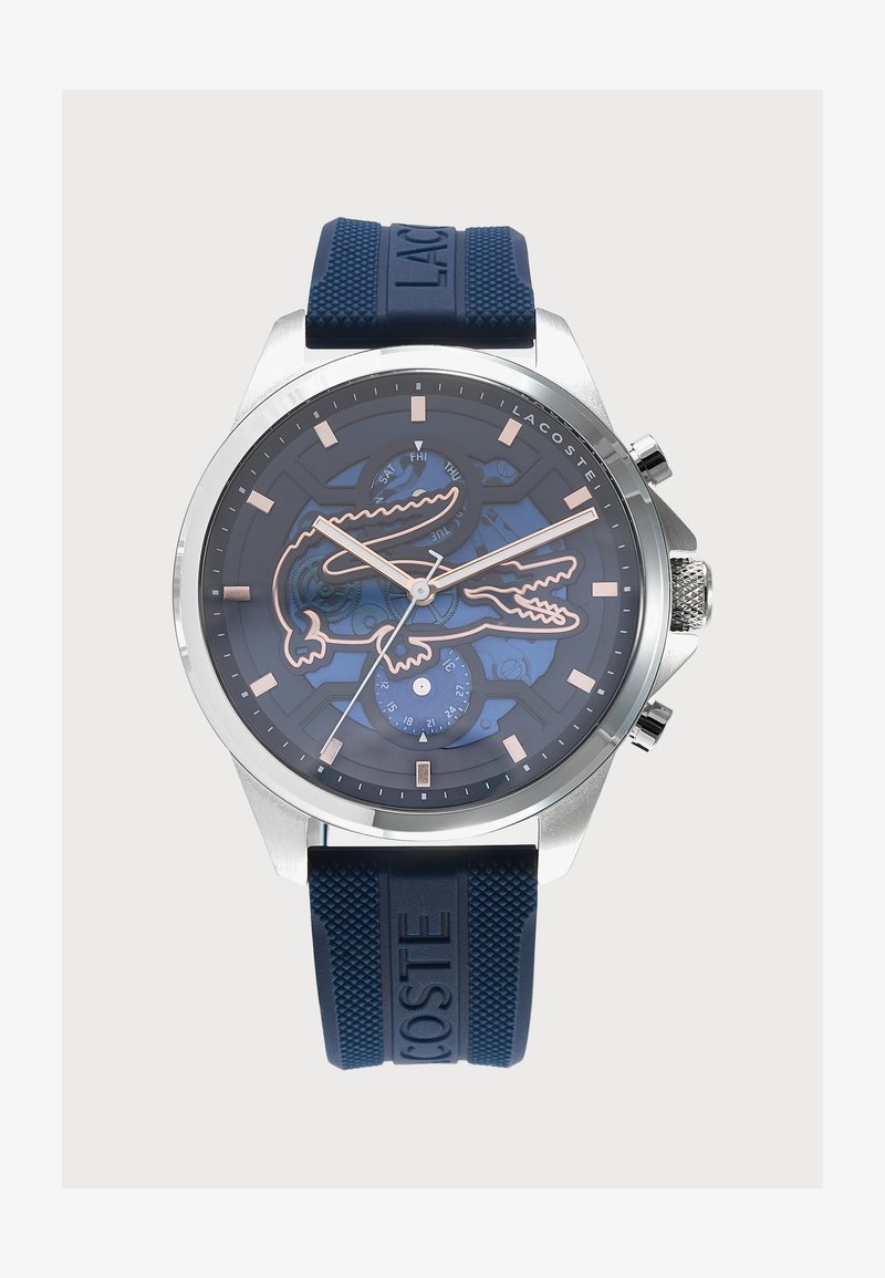 Montre ronde en argent avec un cadran bleu présentant un grand contour de crocodile, des petits cadrans supplémentaires pour la date et le jour, et un bracelet logo texturé bleu.