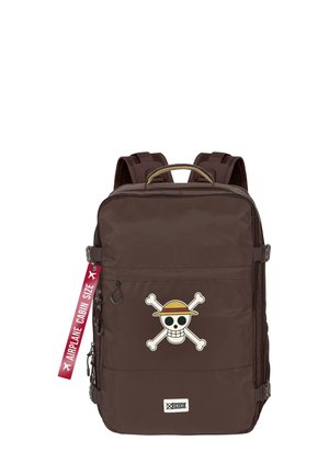 Mochila marrón hecha de un tejido duradero, presenta un gran gráfico de calavera y huesos cruzados, y una etiqueta roja con la inscripción "TAMAÑO DE CABINA DE AIRPLANE".