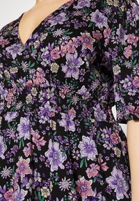 Vestido floral com fundo preto e flores roxas, rosas e verdes, cintura franzida e decote em V profundo. Mangas curtas e bufantes.